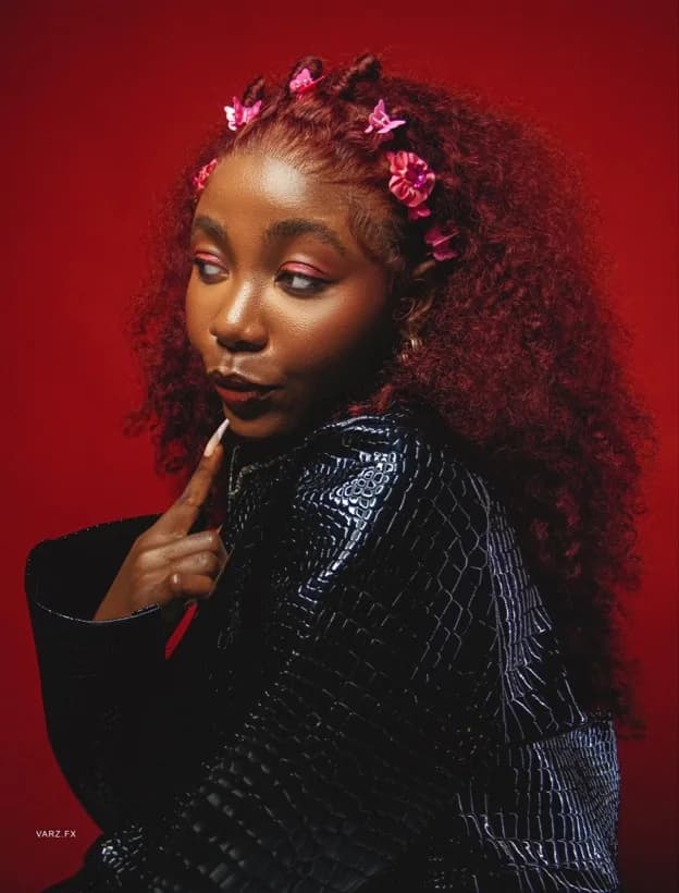 Big Jeanne in a black leather jacket with pink hair clips against a red backdrop